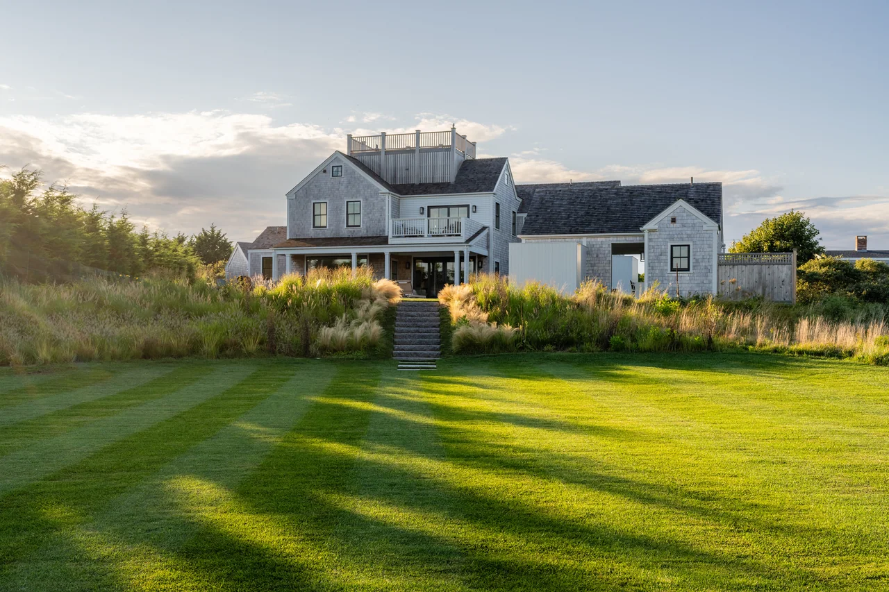 Shingle house sits beyond a lawn and planted garden approach