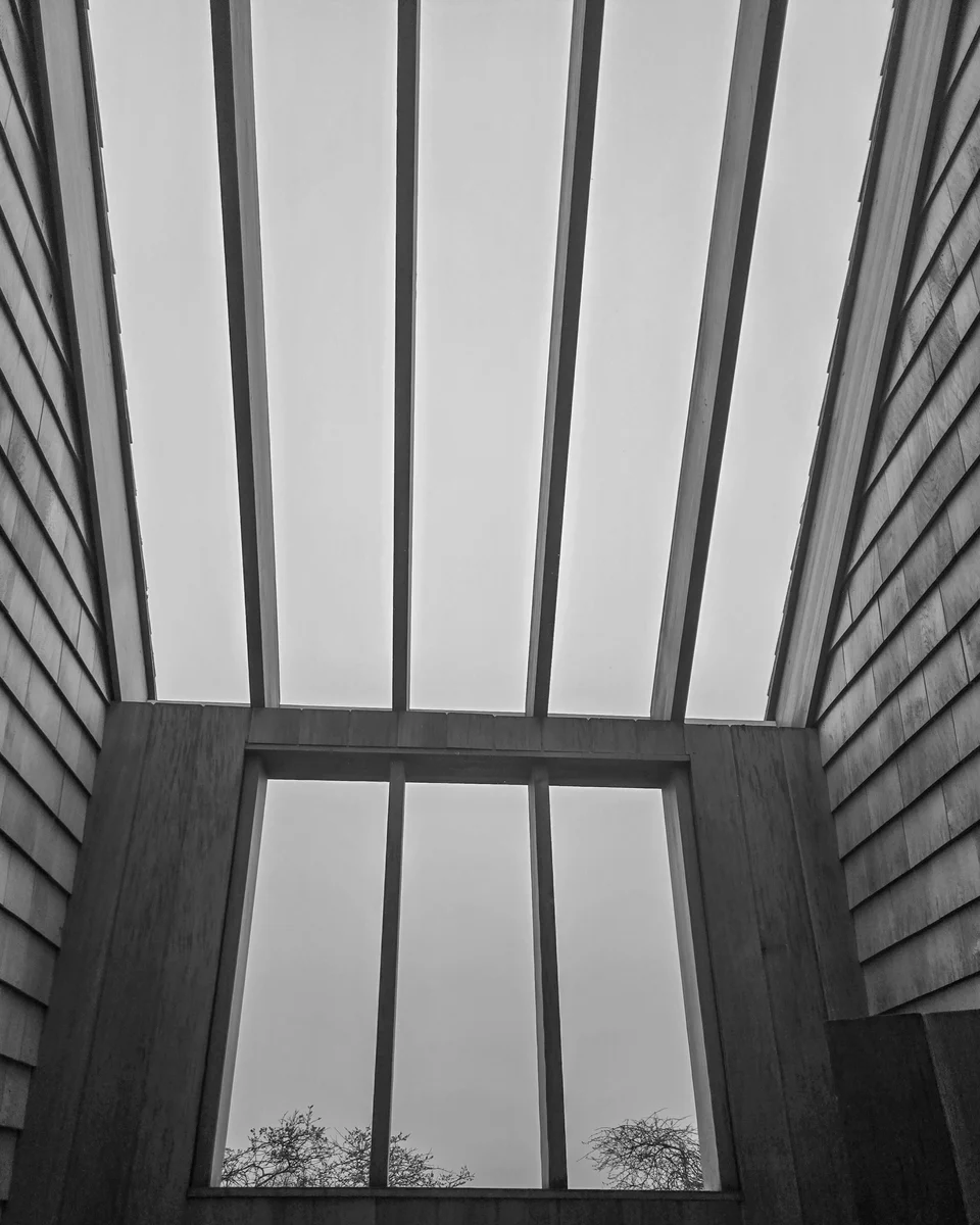 Looking upward through open rafters of a pergola-like structure, with sky visible between the members.