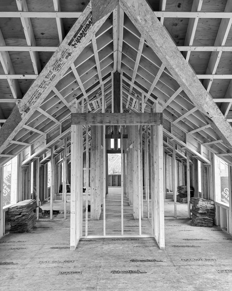 Symmetrical timber roof framing and wall studs reveal the volume beneath a pitched roof.